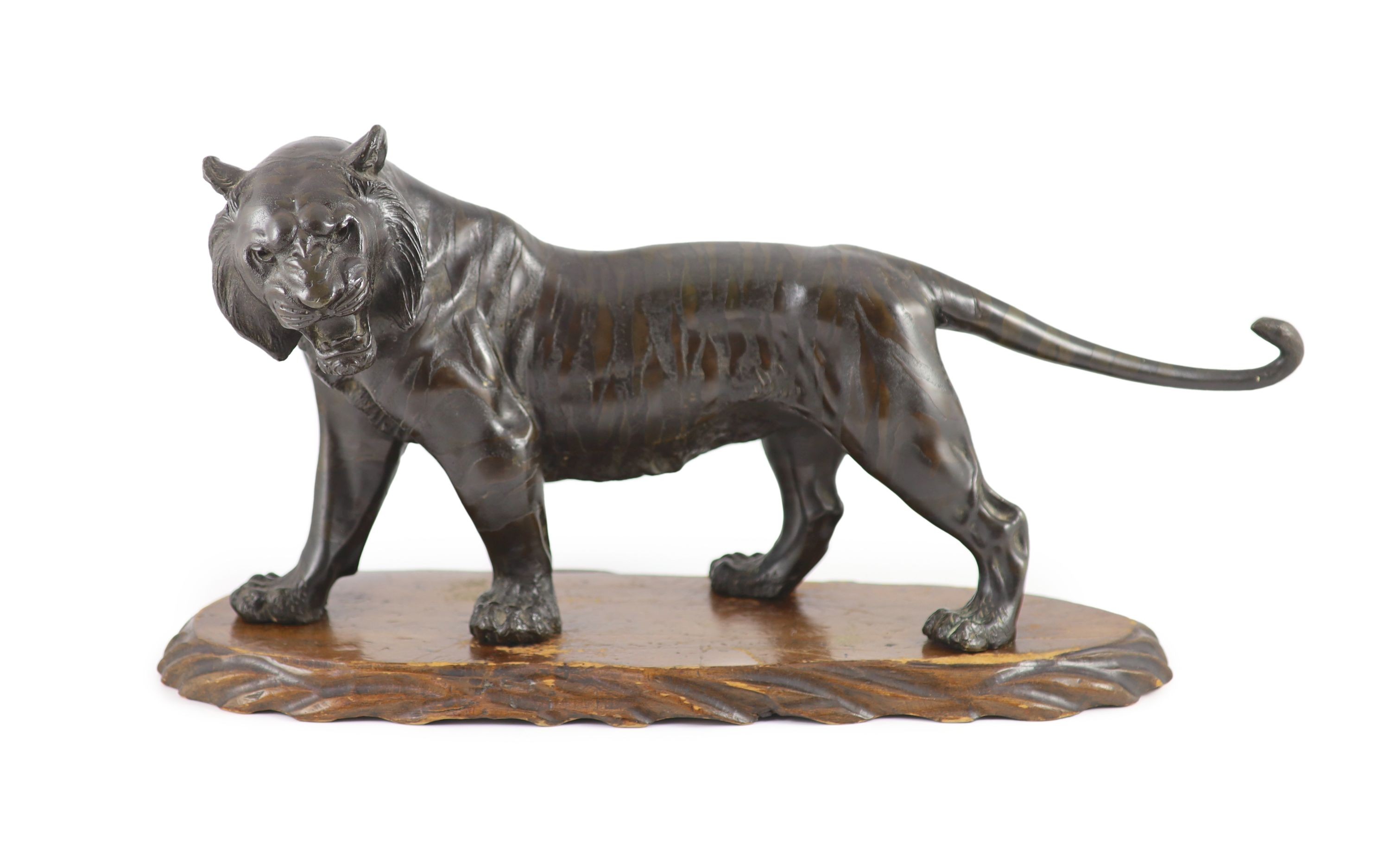 A large Japanese Meiji bronze model of a stalking tiger, Meiji period, 58.5 cm long, wood stand